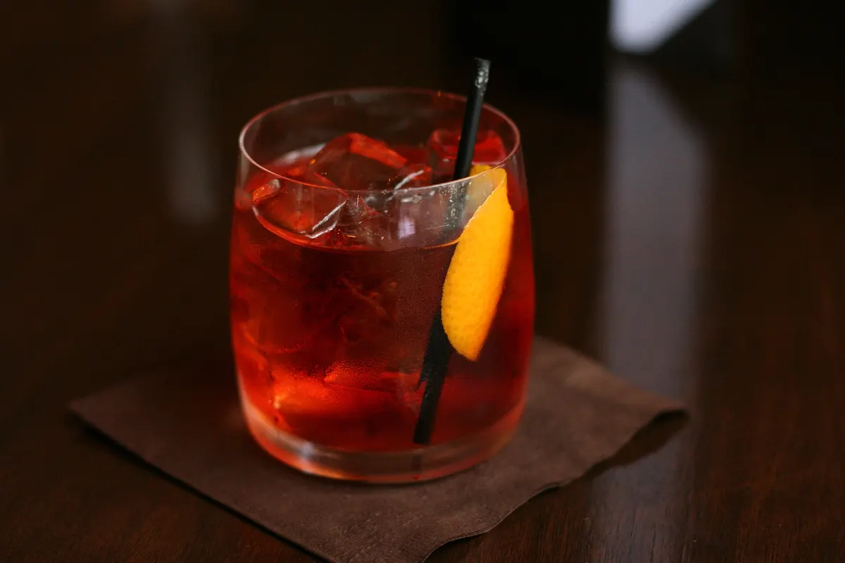A negroni on a dark bar top, lit from one side